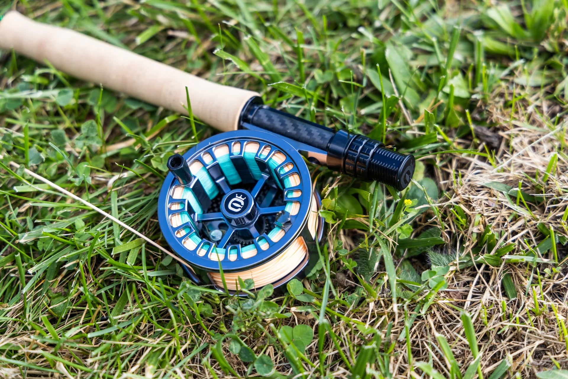 Cortland retro click fly reel in blue anodized aluminum with teal backing line on a cork-handled rod resting in grass