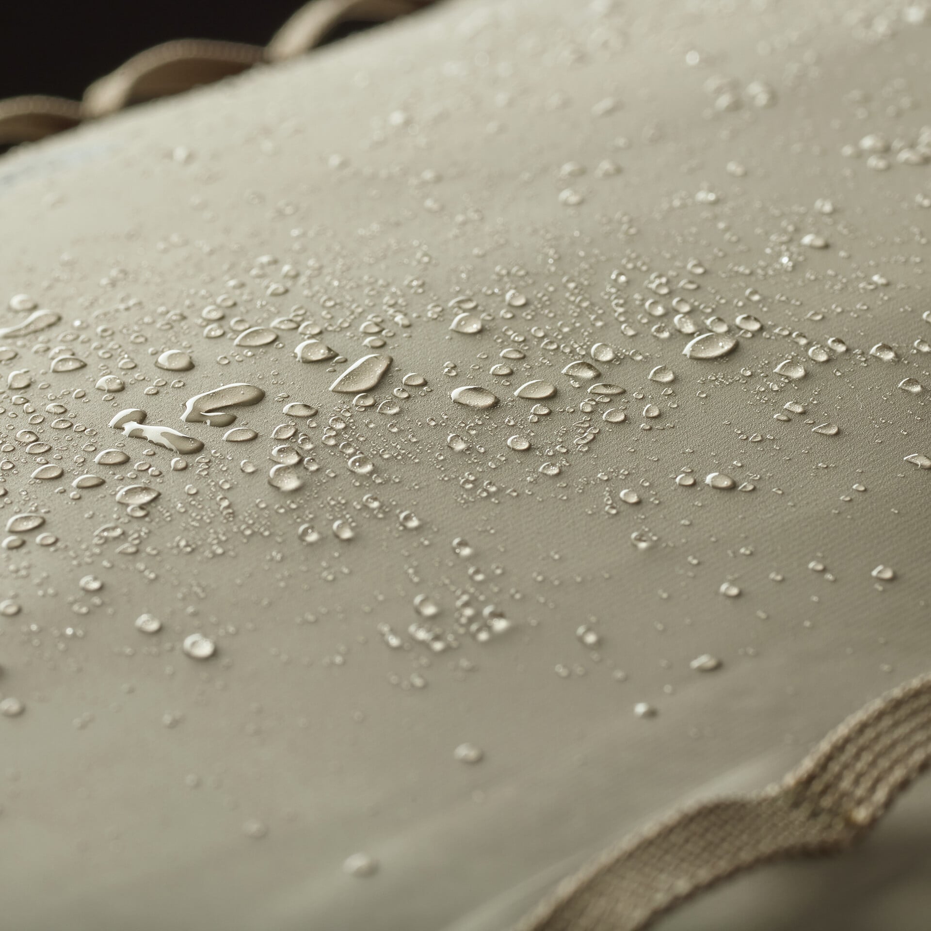 Tan Patagonia roll-top pack fabric close-up with beaded water droplets and tan webbing strap showing waterproof coating