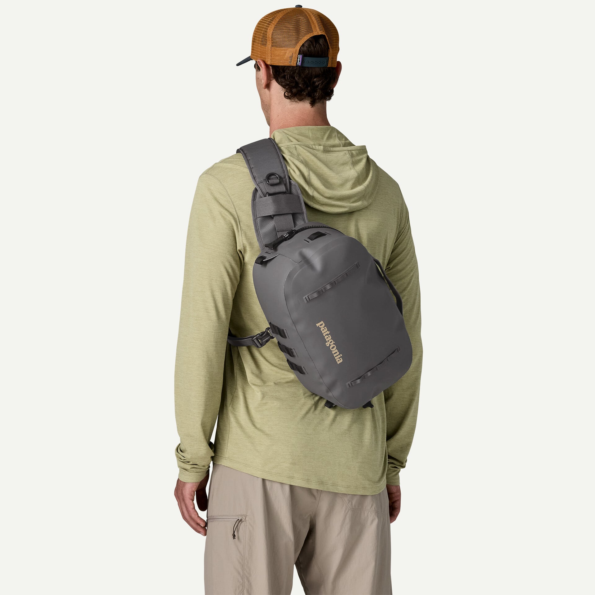Gray Patagonia pack sling backpack with matte waterproof fabric worn over shoulder with olive hoodie