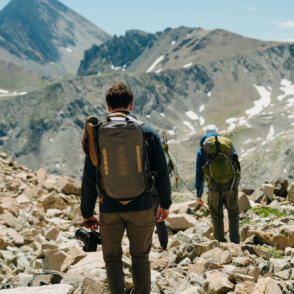 Hikers wearing backpacks traverse rocky mountain terrain with waterproof duffel bags, showcasing outdoor gear durability.
