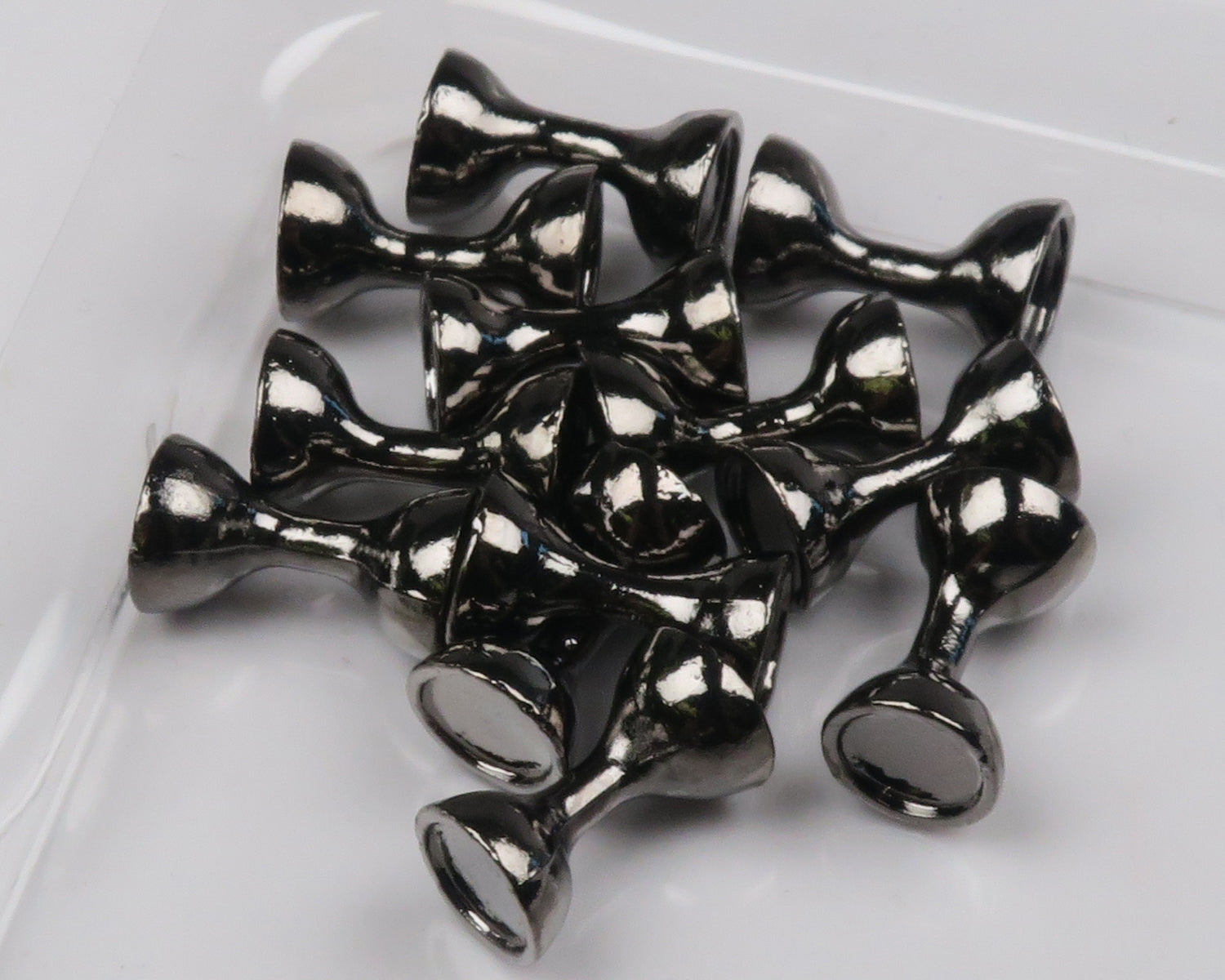 Glossy black tungsten flat-end hourglass eyes for fly tying, metallic low-profile hourglass beads on white surface