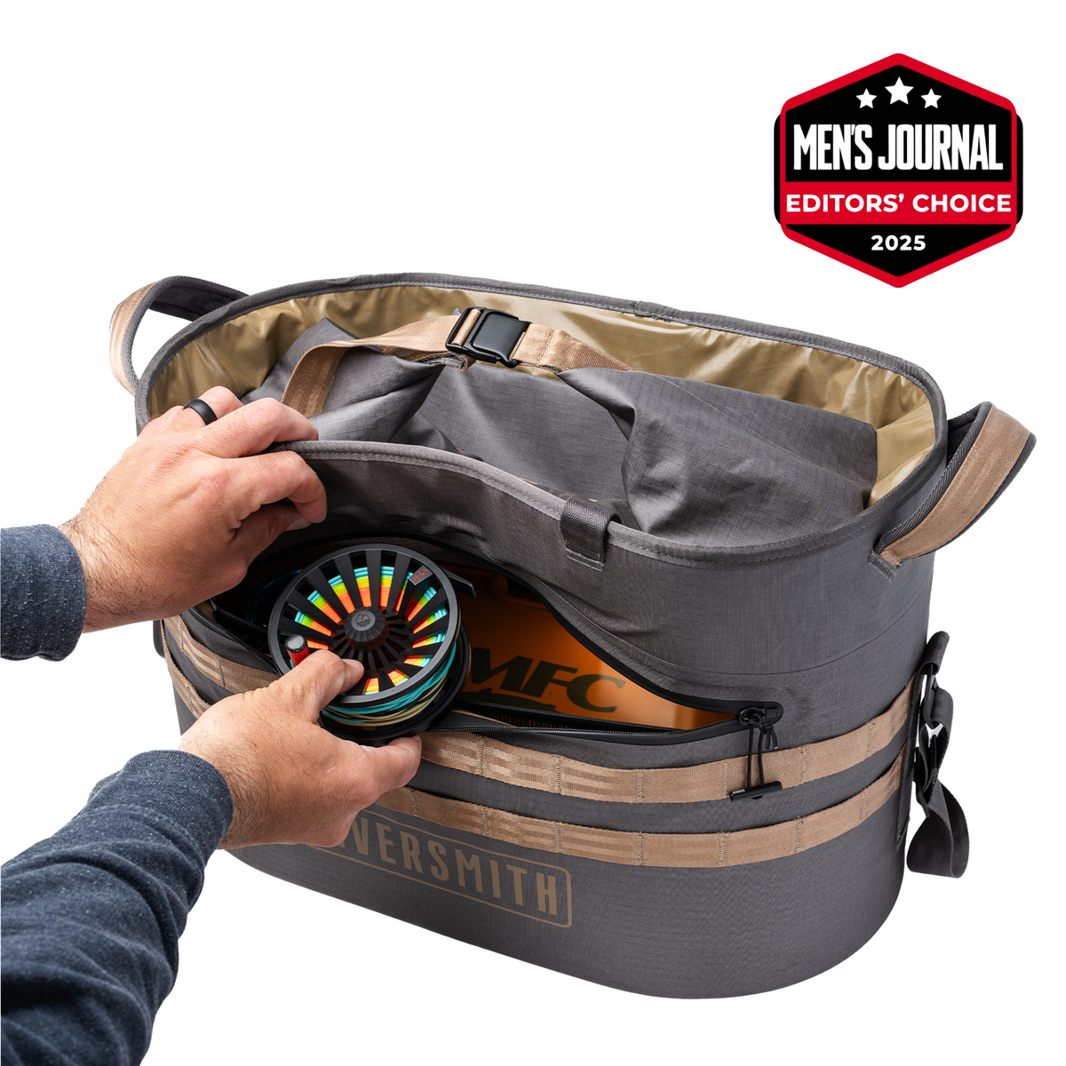 Riversmith Hauler waterproof fishing gear bag with tan and gray design, holding colorful fly reel inside compartment