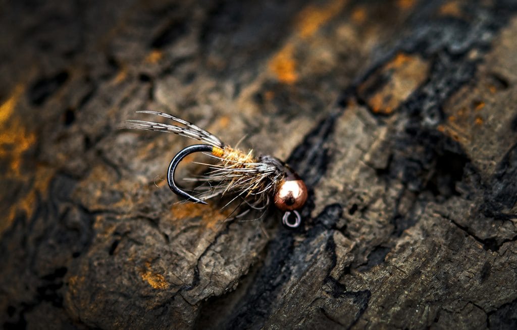 Copper-bead Ahrex mini jig hook with black shank, brown dubbing and speckled feather tail for fly tying