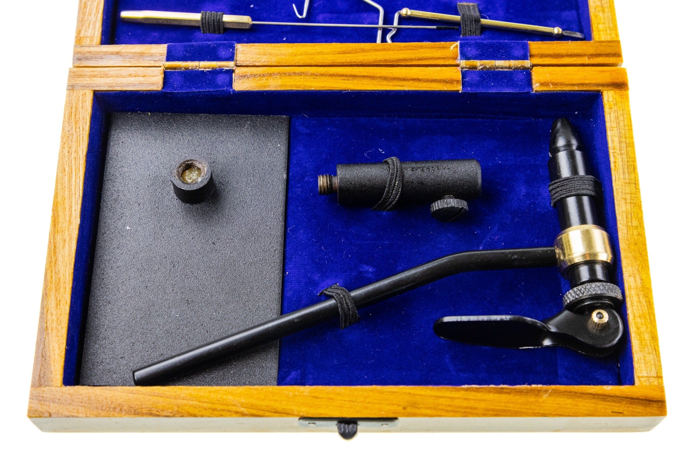Wooden box with blue velvet lining holding black metal fly tying tool kit and pedestal base, brass ring detail