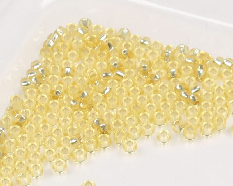 Translucent pale yellow glass beads with silver-lined centers for fly tying, loose pile on white background