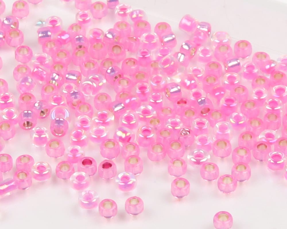 Translucent pink iridescent glass seed beads with center holes scattered on white background for fly tying