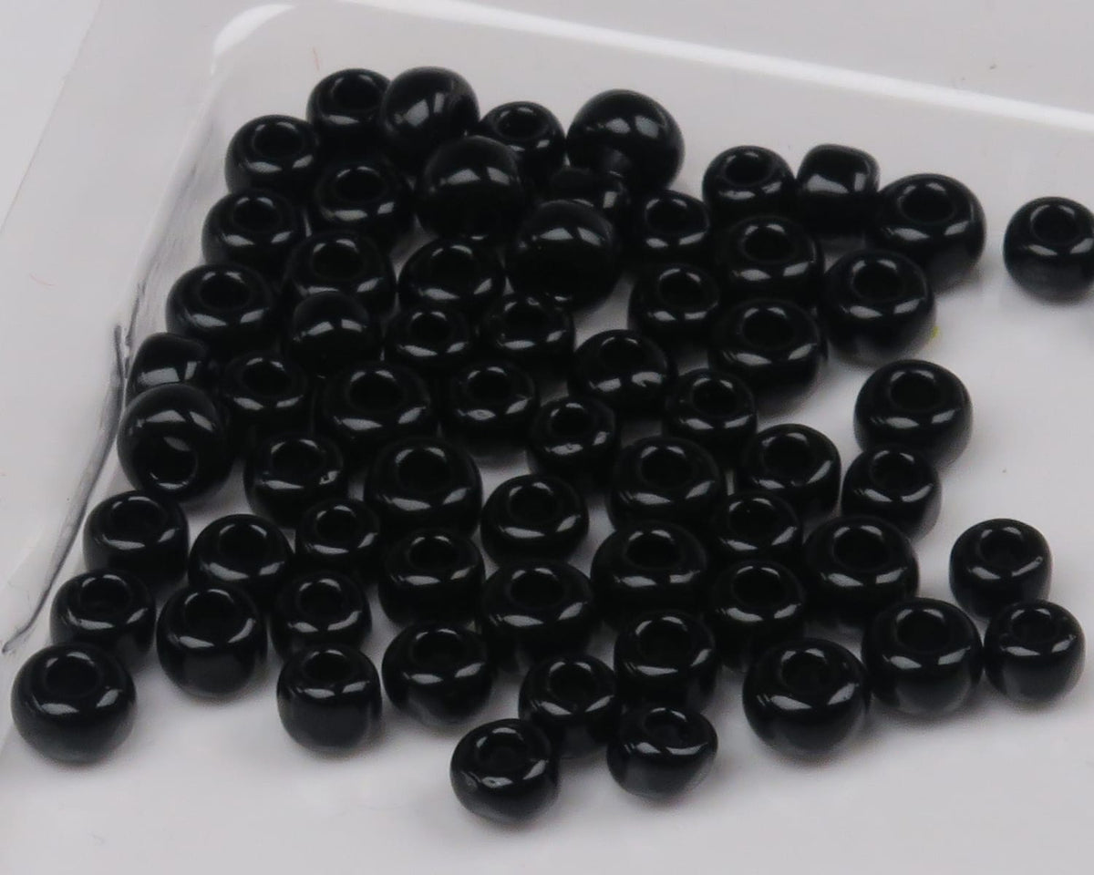 Black glossy round glass beads with large center holes scattered on white background, fly tying beads