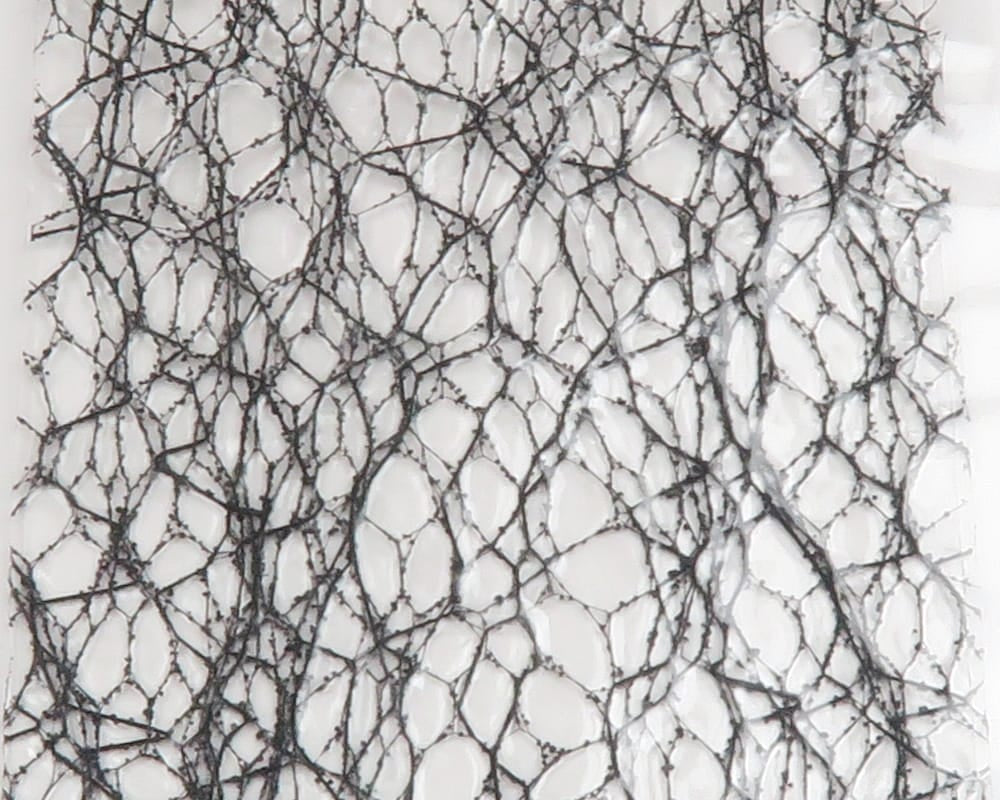 Black web-like gummy wings material with irregular open cells and thin rubbery strands on white backing, fly tying