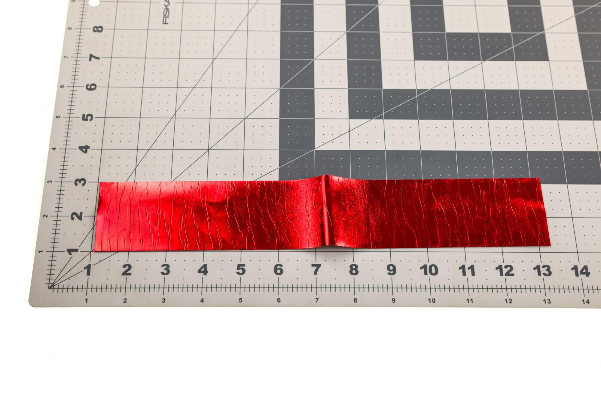Red metallic Chocklett's Sili Skin strip with crinkled texture laid on a gridded cutting mat, fly tying material