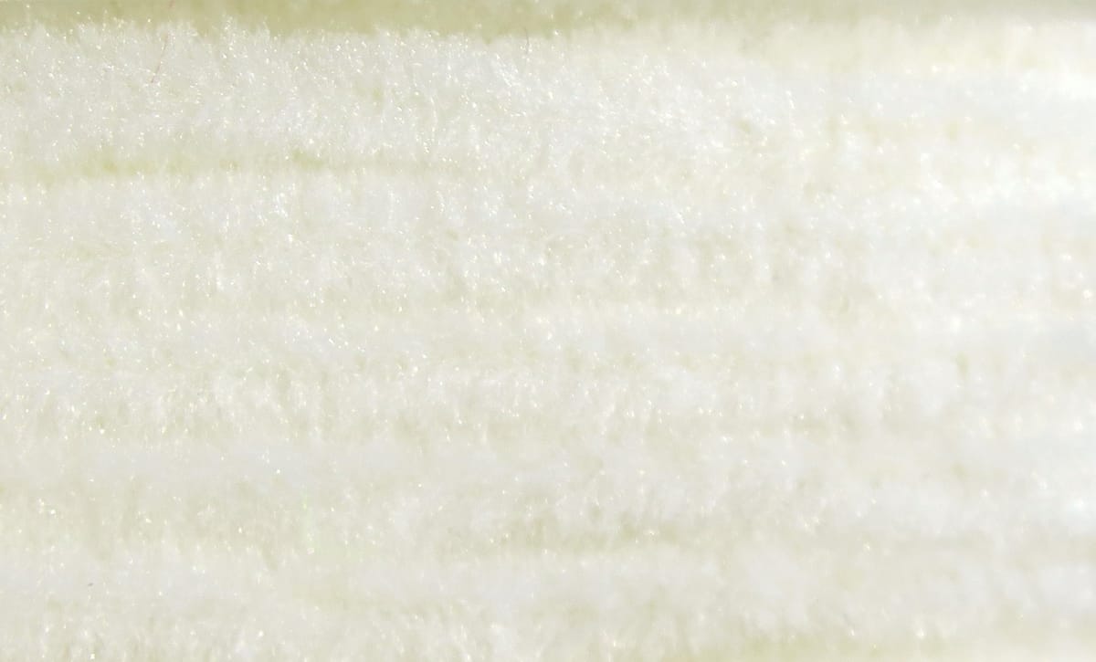 White Hareline chenille close-up showing soft fuzzy fibers with subtle sparkle, fly tying material.