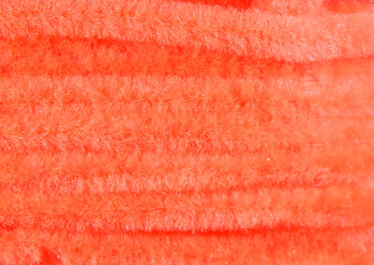 Bright orange Hareline chenille close-up showing soft fuzzy pile and parallel ridges for fly tying