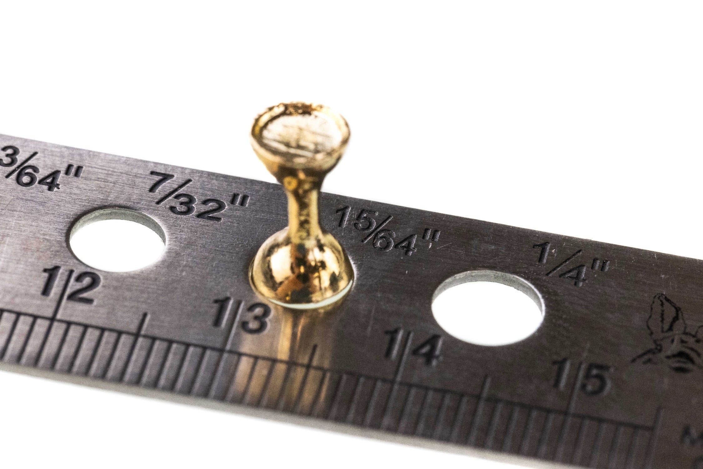Gold flat-end tungsten hourglass fly-tying eye with polished metallic finish resting on ruler gauge