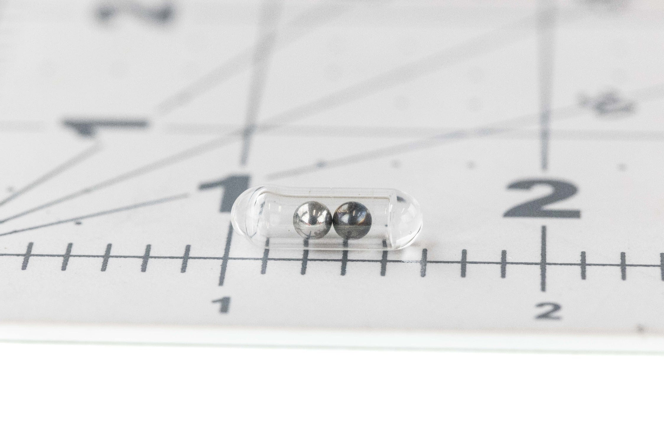 Hareline fly tying glass rattler clear capsule with two silver beads on ruler background