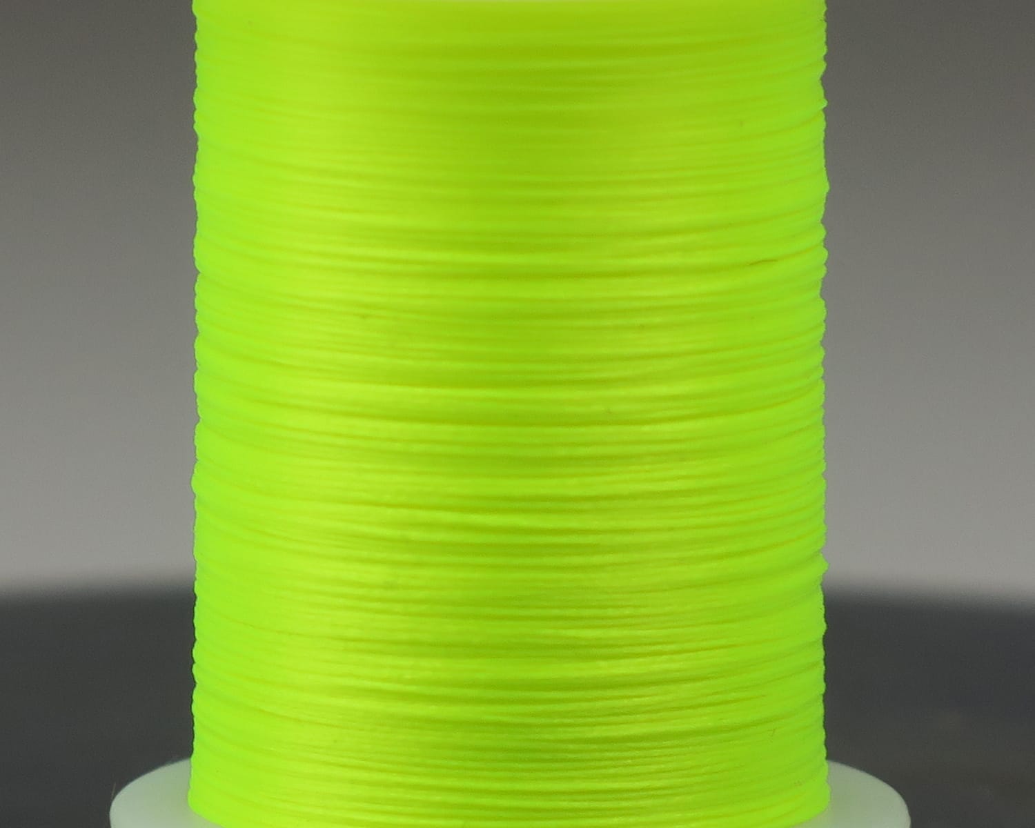 Fluorescent chartreuse Glo-Brite fly tying floss tightly wound on a white spool, smooth synthetic thread