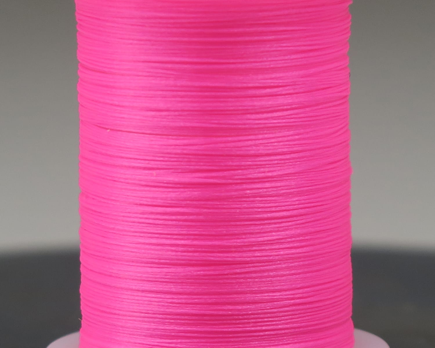 Hareline Glo-Brite neon hot pink synthetic fly tying floss spool, close-up showing smooth shiny wound thread