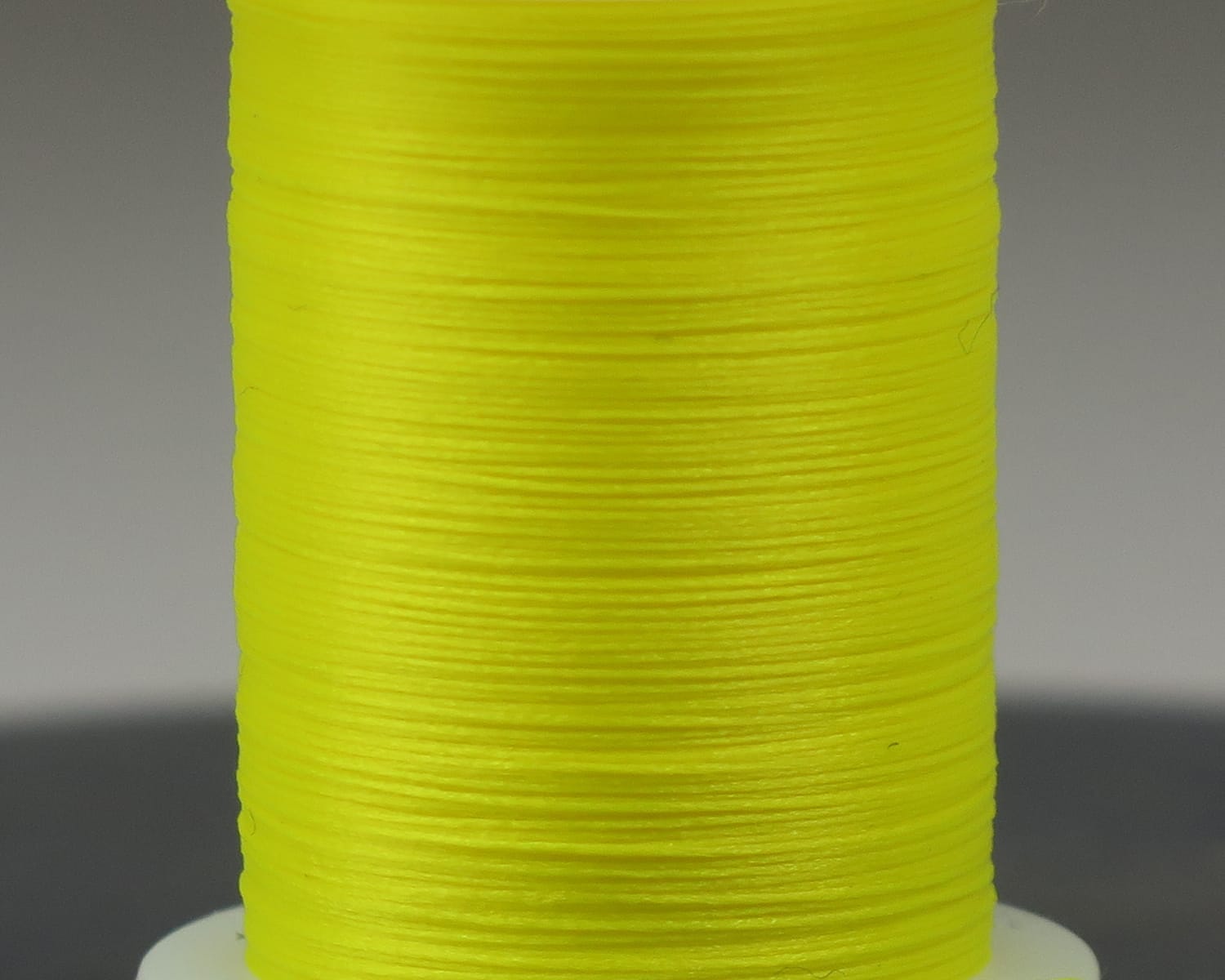Fluorescent yellow nylon Glo-Brite floss spool for fly tying with tightly wound smooth thread
