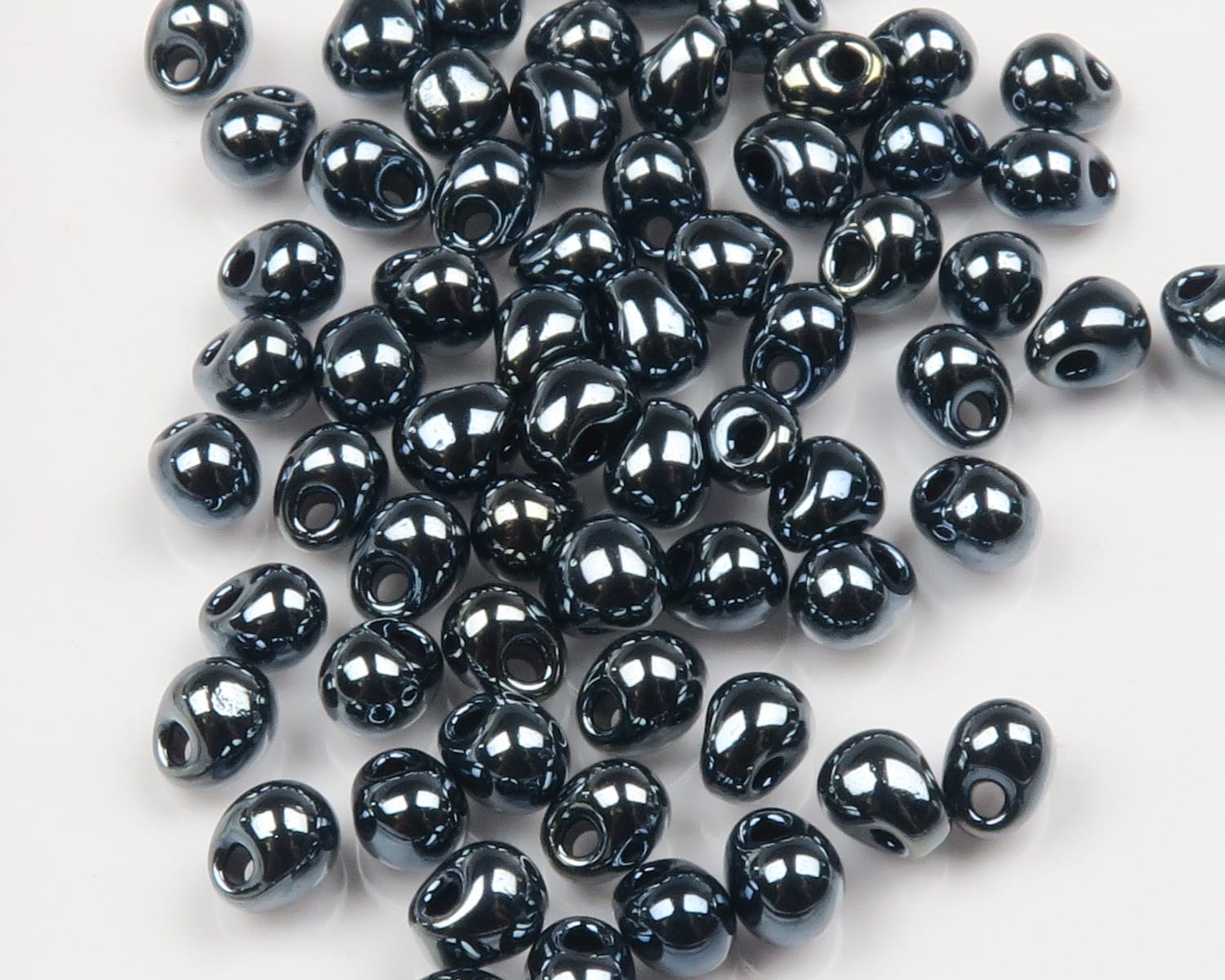 Glossy metallic black humpback glass beads with teardrop shape and threading holes, scattered for fly tying.