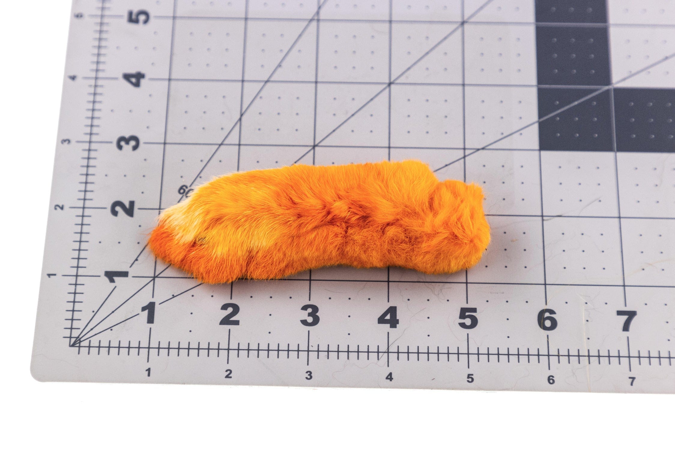 Bright orange Para Bunny feet fur strip for fly tying, soft synthetic rabbit fur patch on gridded cutting mat