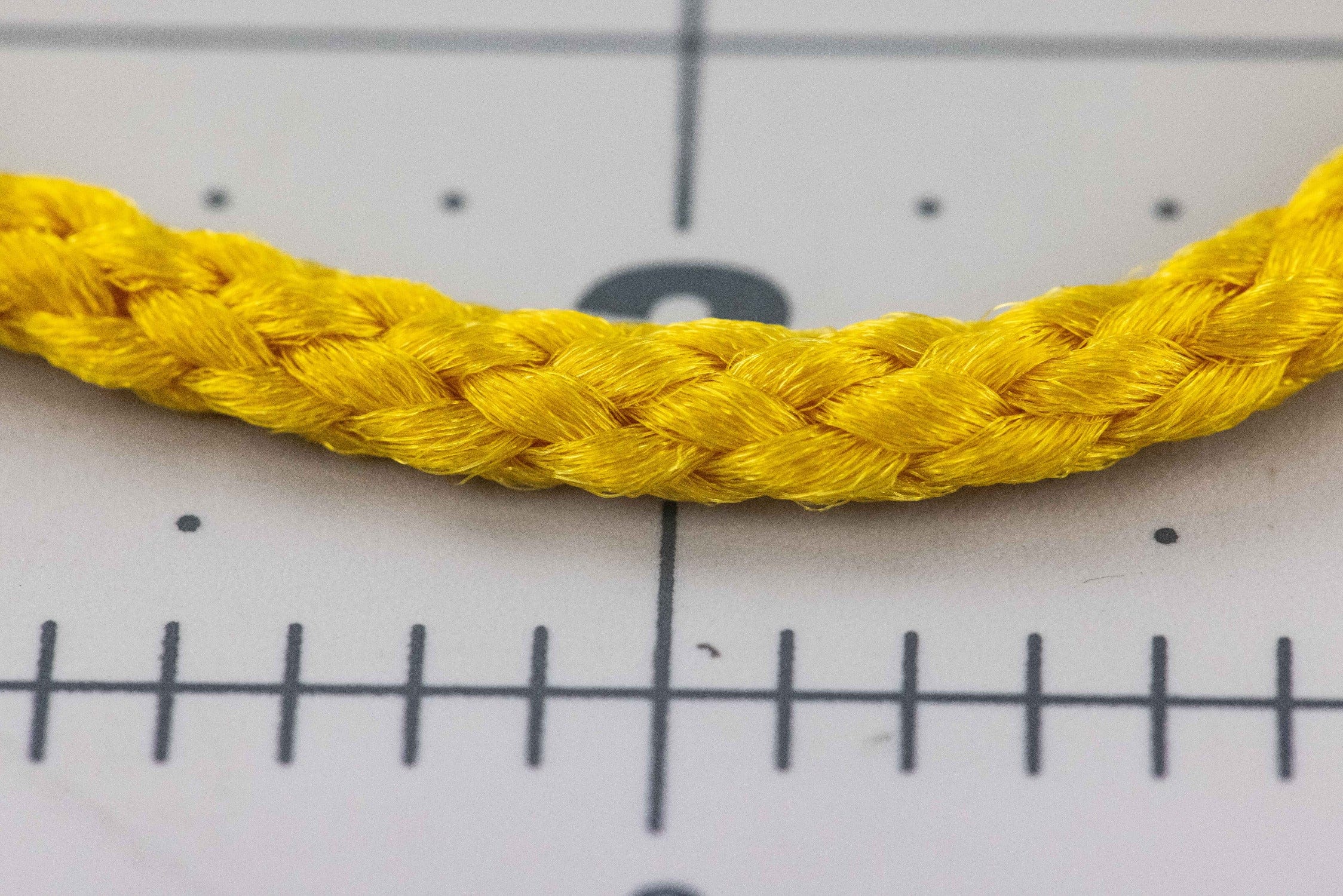 Hareline bright yellow synthetic braided Poly Pro cord with shiny fibers for fly tying on a measurement grid