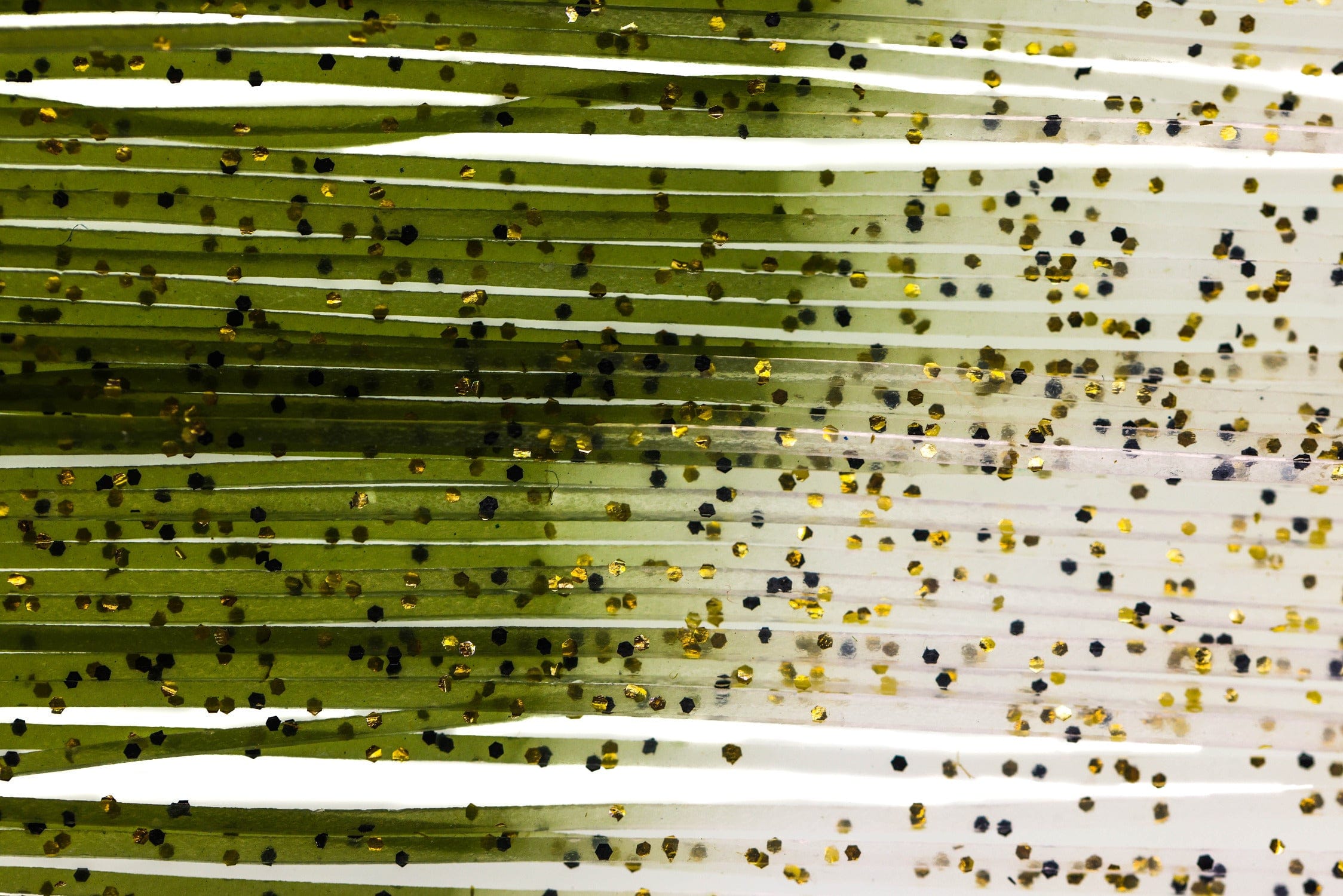 Olive-green translucent rubber Shrimpy Crabby Legs strands with black and gold hex glitter flakes for fly tying