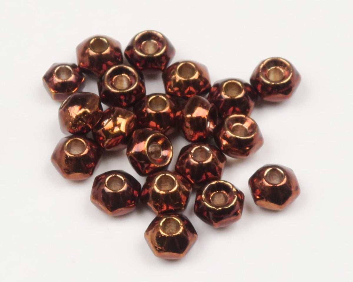 Copper metallic faceted tungsten fly nuts with central holes for fly tying, small round bead weights on white background