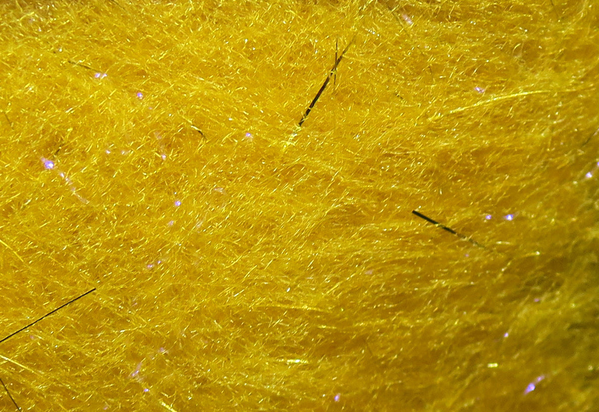 Bright golden yellow synthetic dubbing fibers with iridescent flash and scattered black guard hairs for fly tying