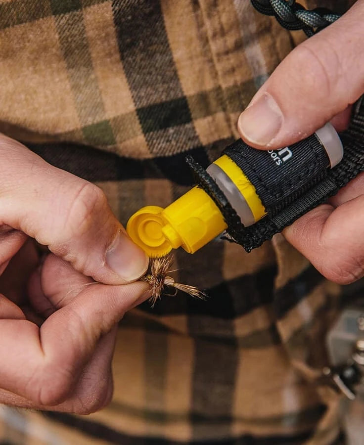 Hands using a yellow plastic Loon Caddy with flip cap in a black nylon sheath to apply material to a brown fly - fly-tying