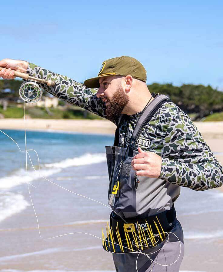Angler wearing waist-mounted Loon Flexi Stripper black plastic stripping basket with yellow flex prongs, fly fishing on beach
