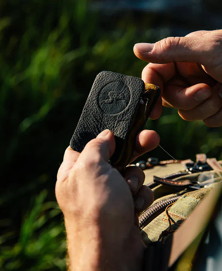 Hands holding black textured amadou patch with embossed Loon logo and thread, leather-style fly tying accessory