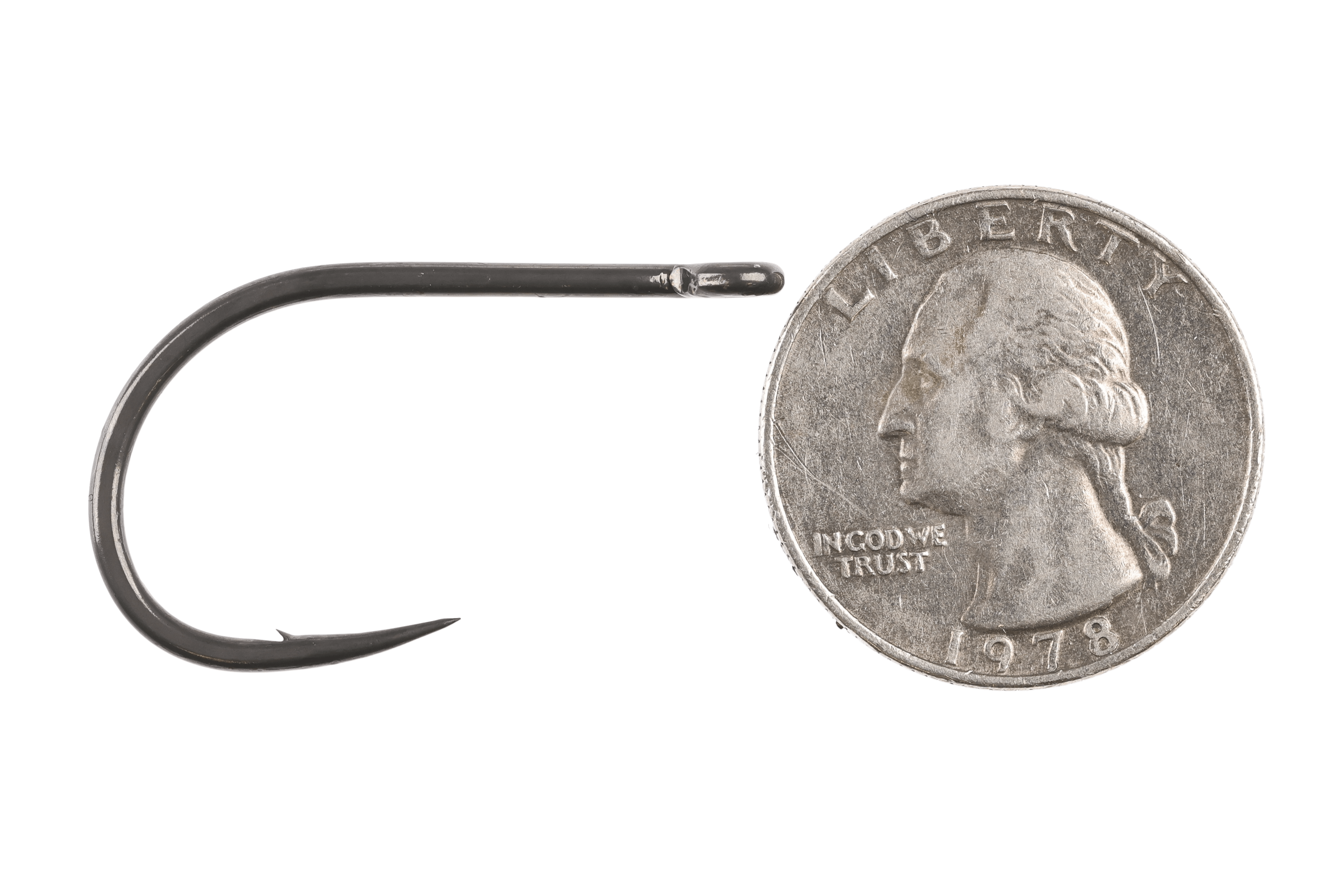 Mustad black nickel big-game fly hook, wide curved heavy shank, sharp barbed point and turned eye beside quarter scale