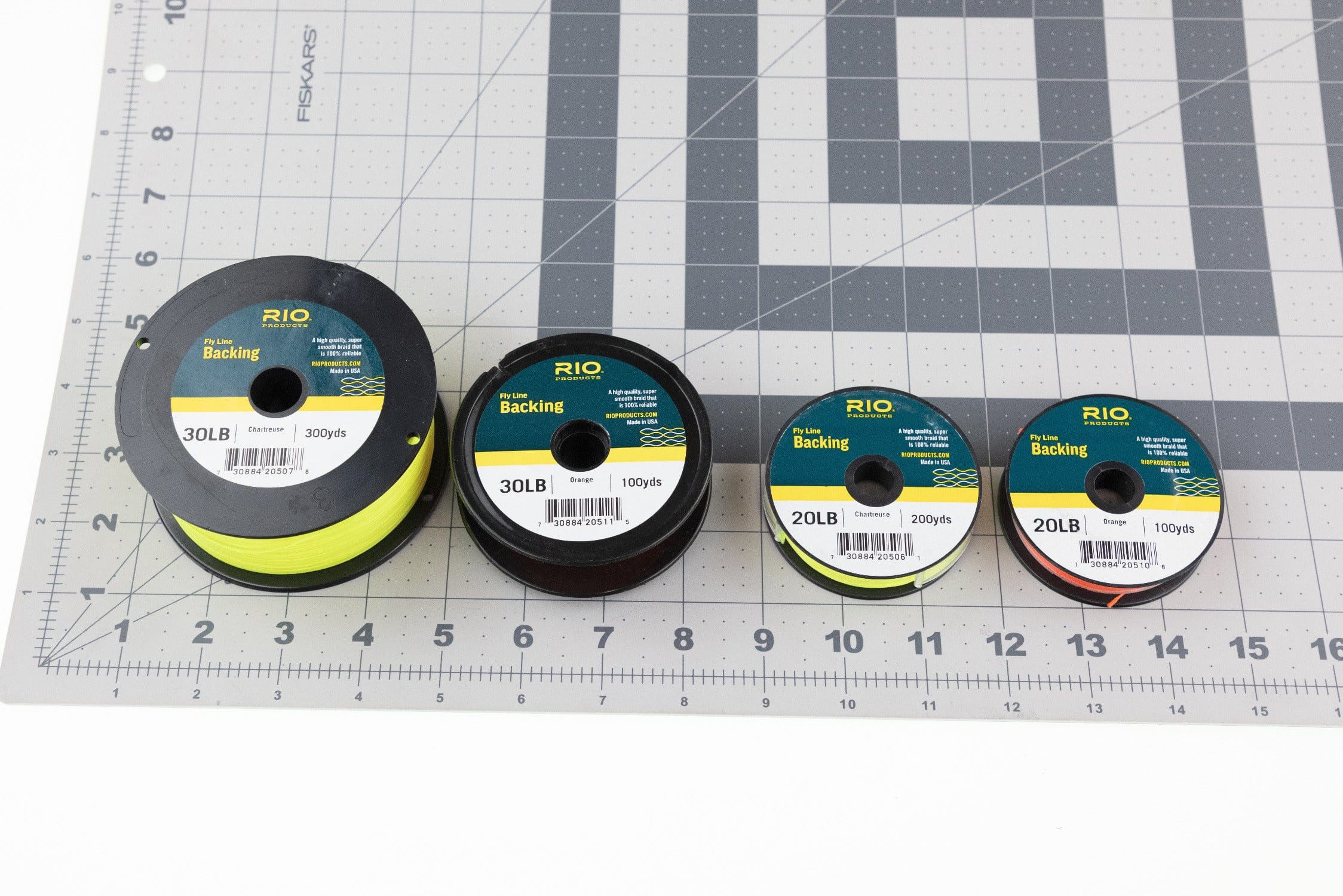 Four Rio Dacron fly line backing spools in chartreuse and orange on a gray cutting mat with ruler grid
