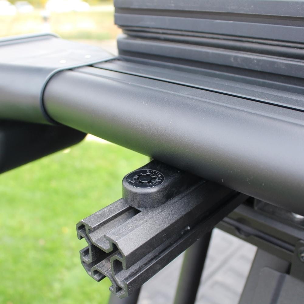 Black T-track mount accessory installed on aluminum roof rail system with green grass background visible