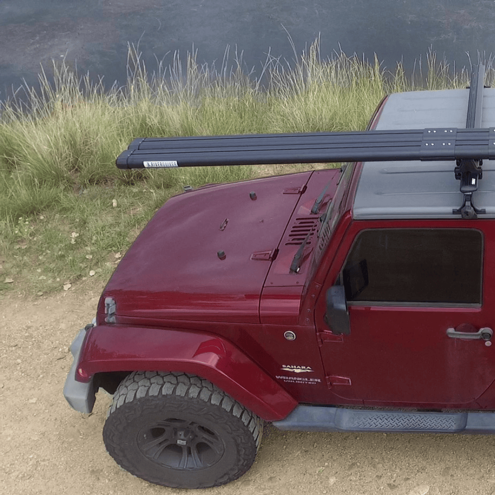 Red Jeep Wrangler with black roof rack extension kit mounted on top near water and grass