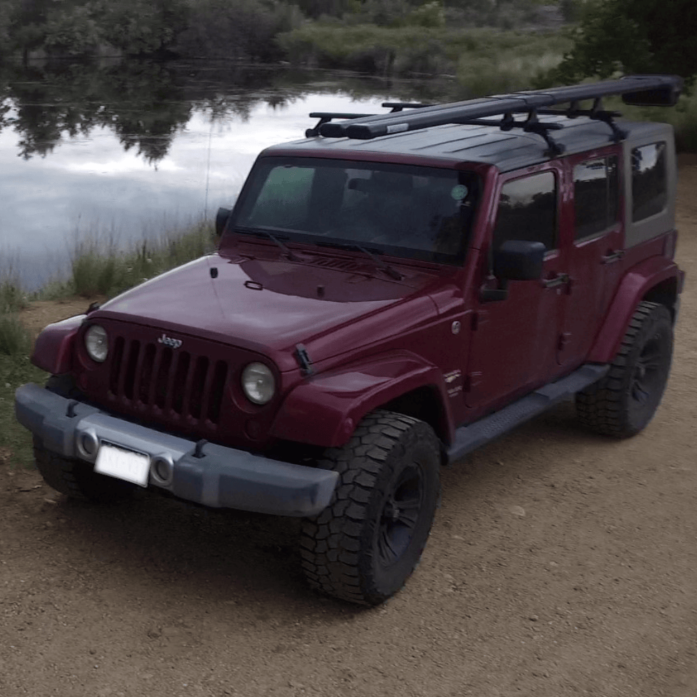 Maroon Jeep Wrangler with black roof rack extension kit parked by riverside