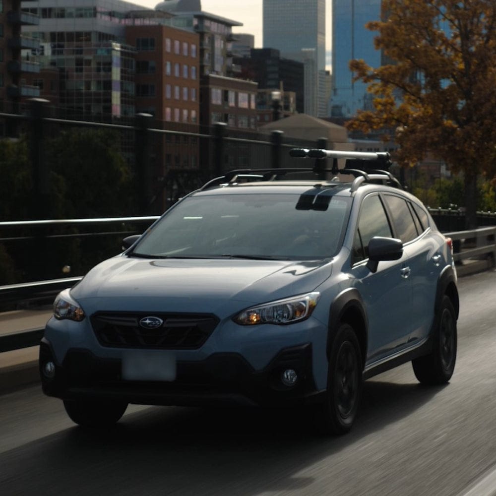 White Subaru Crosstrek with roof rack driving on urban bridge with city skyline background
