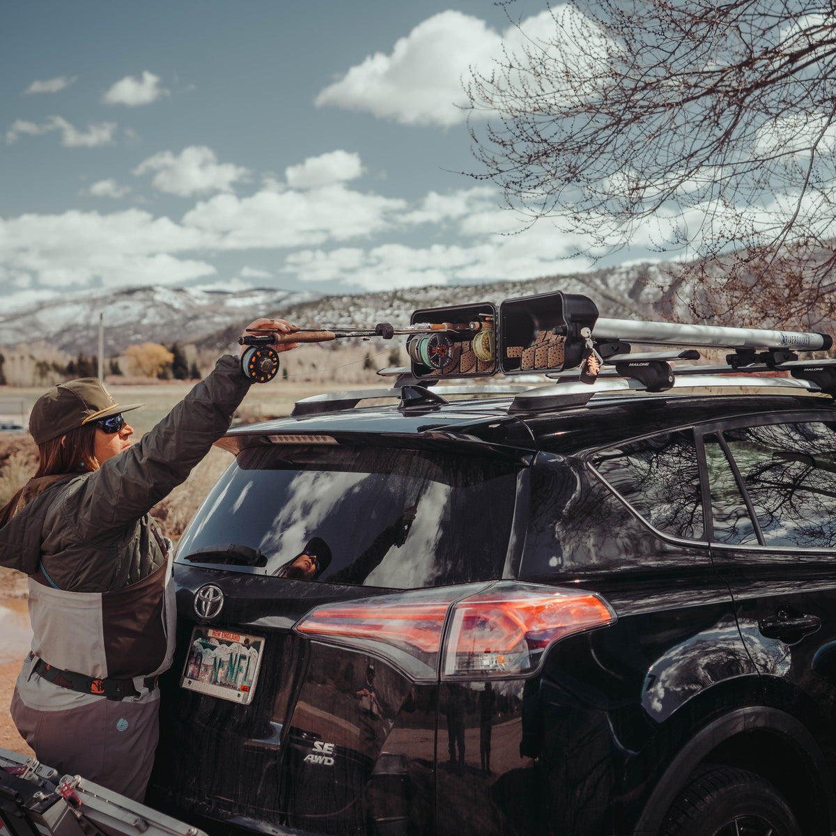 Woman securing Riversmith ShortCut fishing rod rack on vehicle roof with fly rods and gear mounted