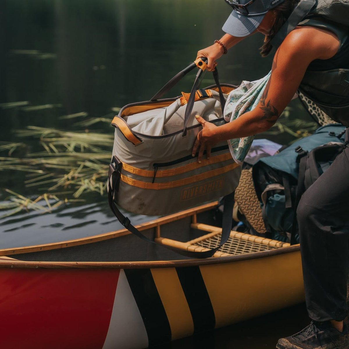 Riversmith The Hauler waterproof tote bag in tan and orange straps being held on a kayak deck near water