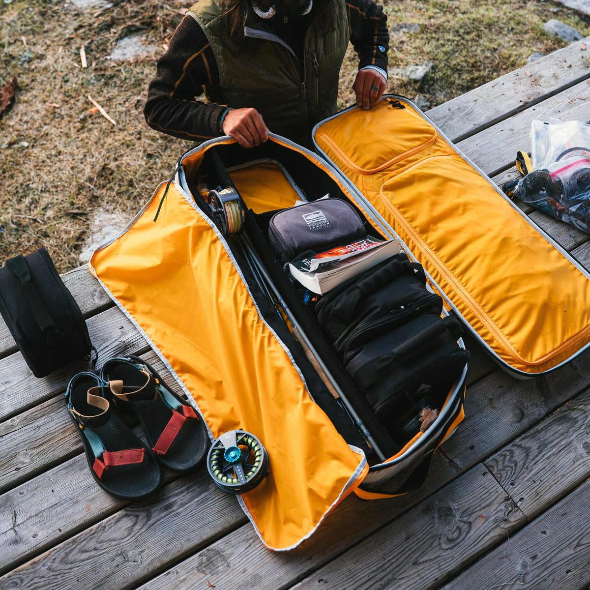 Yellow Riversmith Travel Pack fly fishing bag open on wooden dock with gear organized inside, showing durable storage