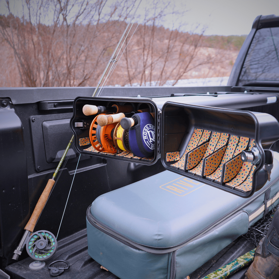 Riversmith Truck Bed River Quiver fishing rod rack with orange and blue reels in truck bed displaying organized storage