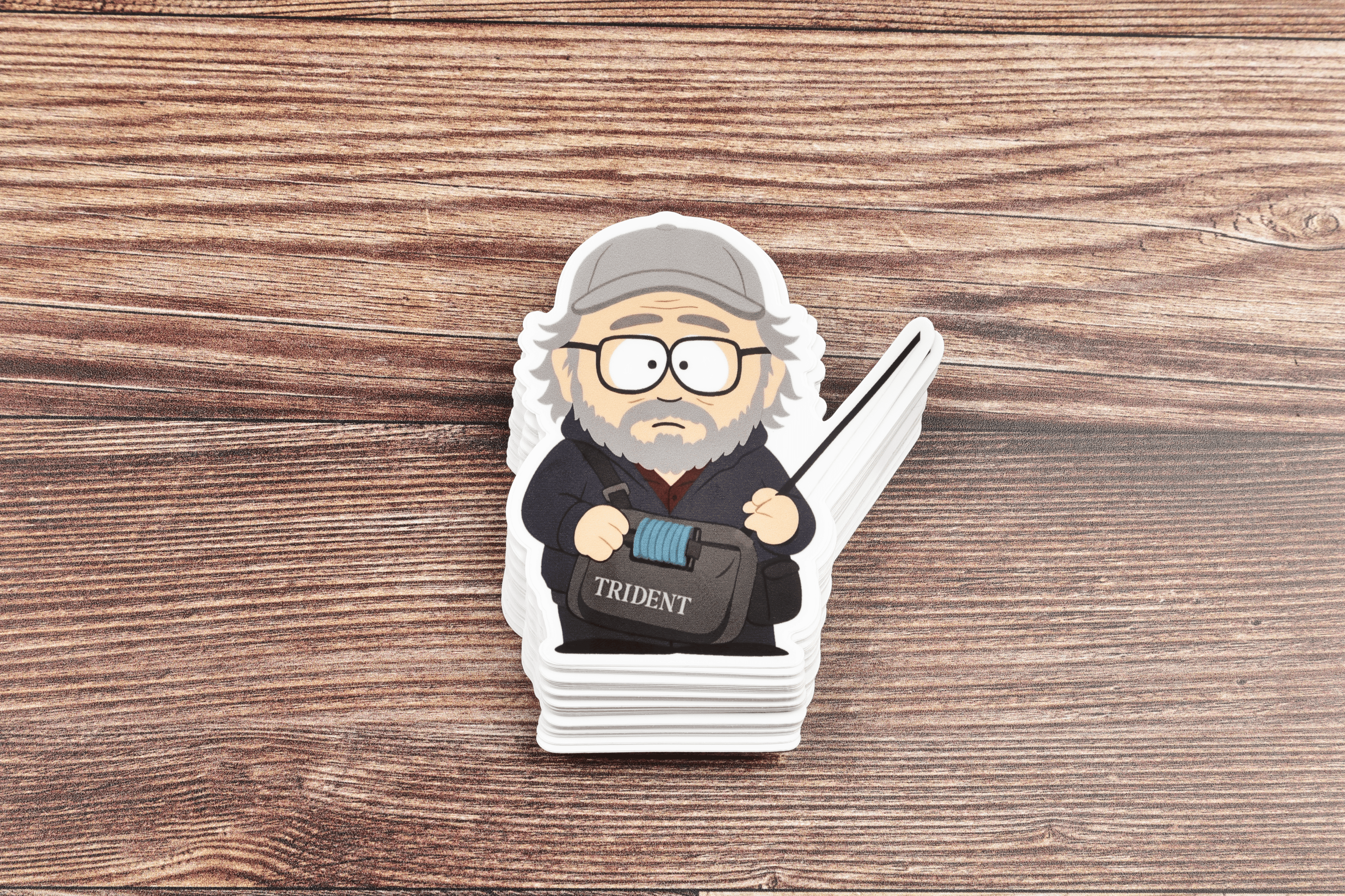 Die-cut vinyl sticker of cartoon bearded man with gray cap and glasses holding Trident bag on wood background