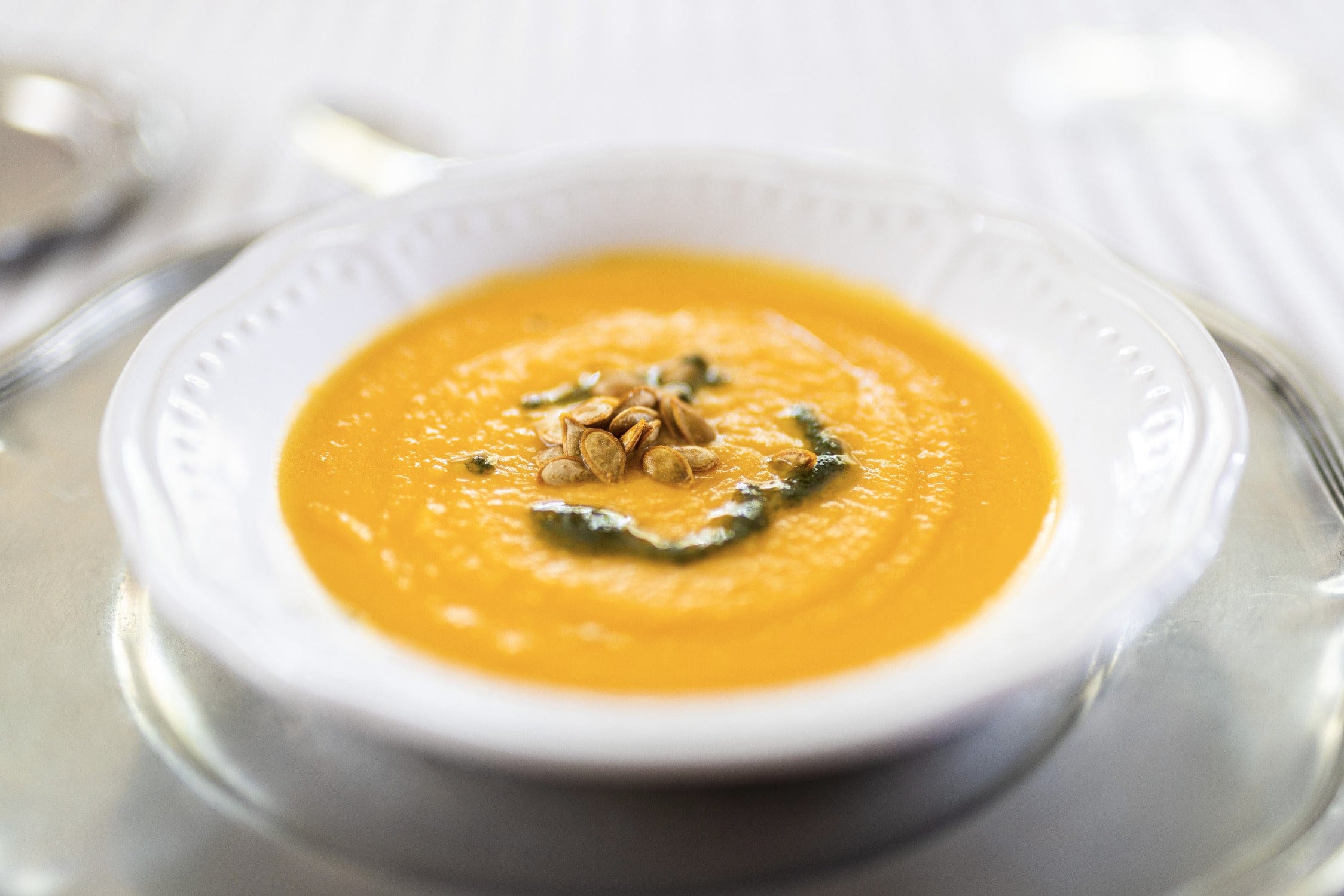 Creamy orange pumpkin soup with toasted seeds and basil oil in white ceramic bowl on plate - safari trip dining