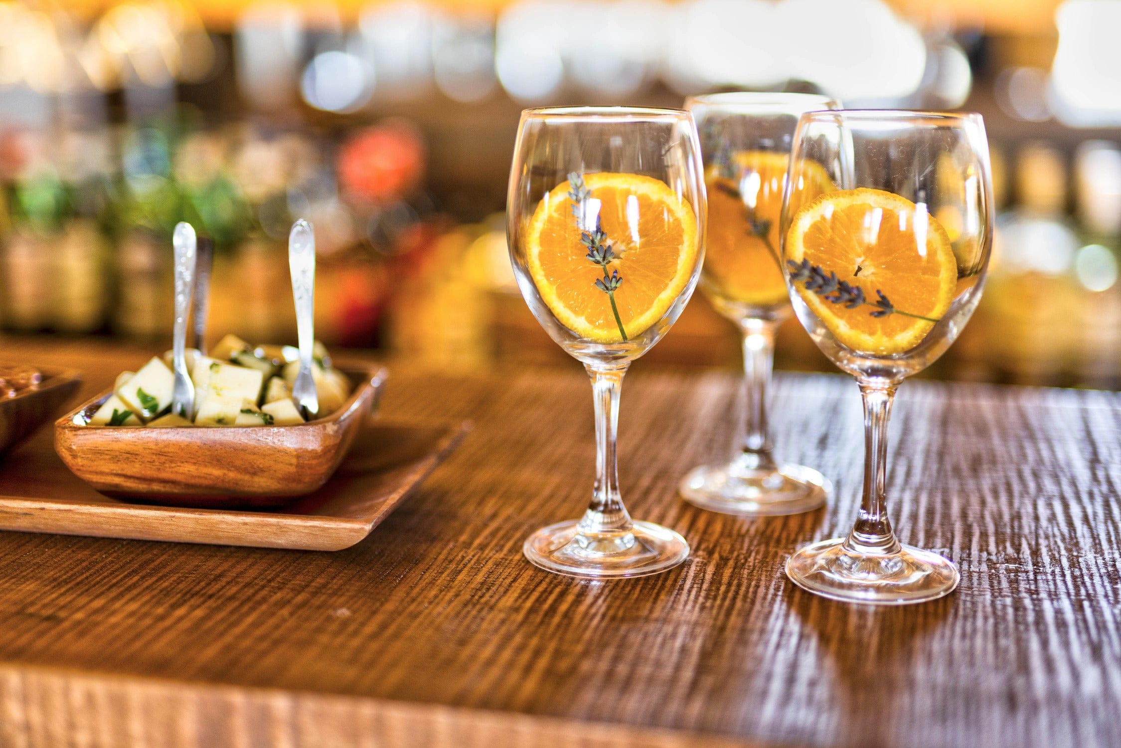 Clear wine glasses with bright orange slices and lavender on a rustic wooden table, cheese bowl nearby — safari trip