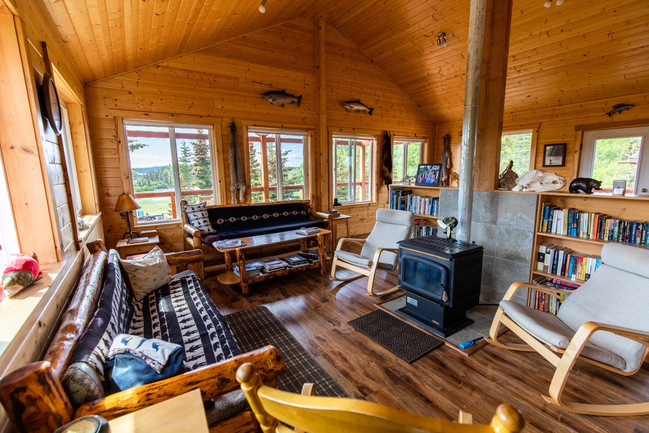 Cozy Copper River Lodge interior with warm pine walls, log furniture, wood stove and forest-and-lake view windows