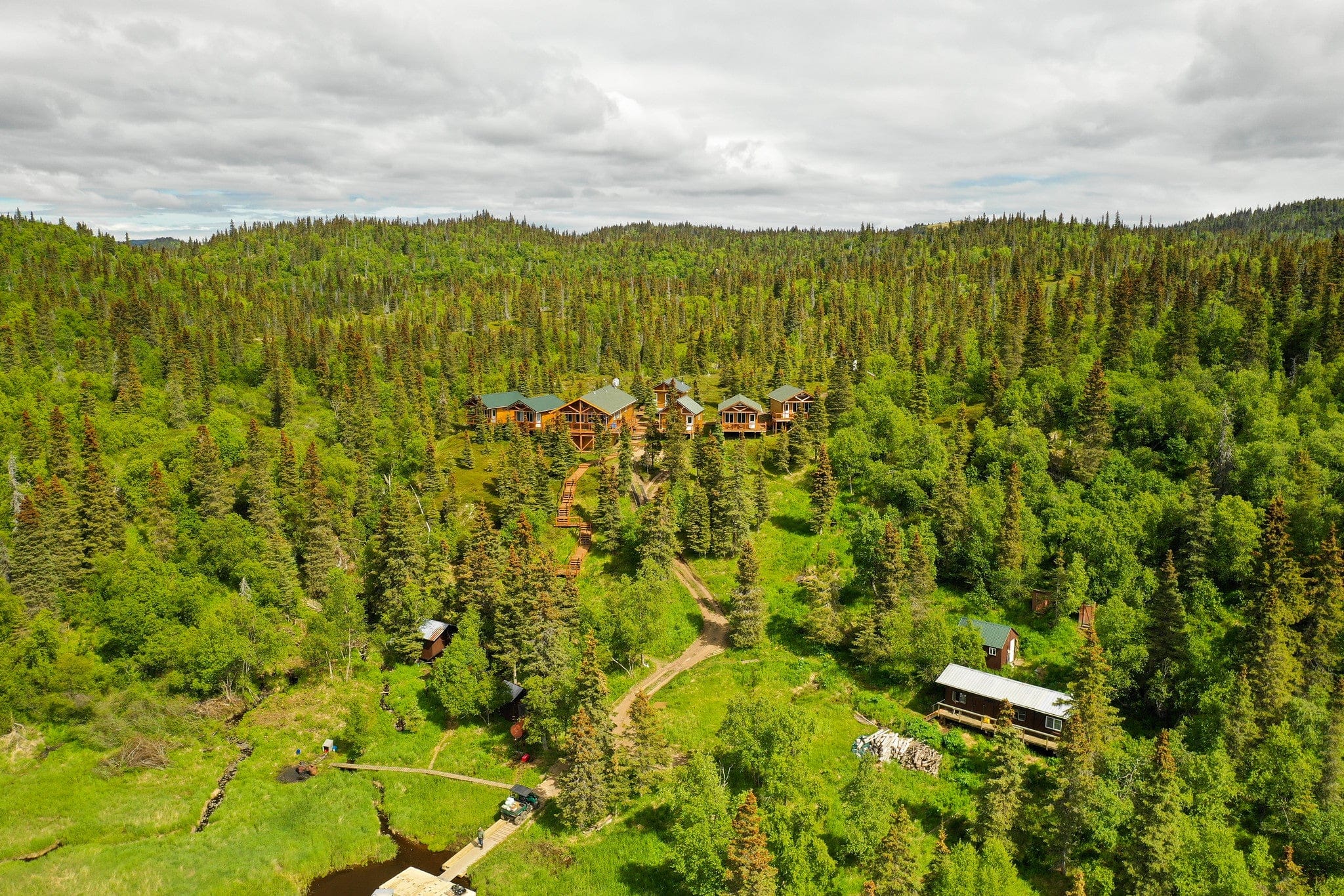 Copper River Lodge cluster of wooden log lodges with green metal roofs by a dock, surrounded by dense green spruce forest