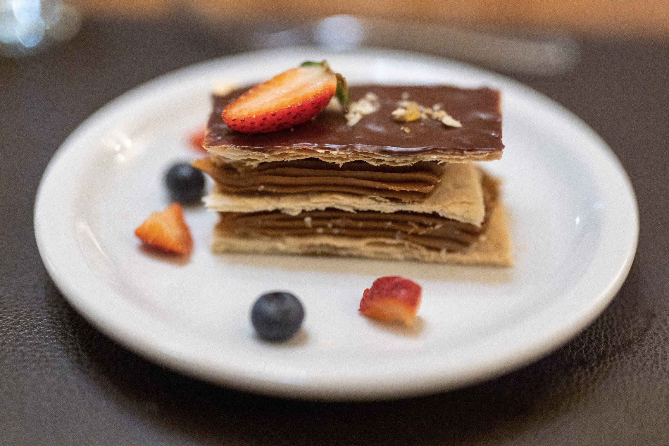 Chocolate-glazed mille-feuille layered pastry with sliced strawberry and blueberries on white plate — Jurassic Lake Lodge