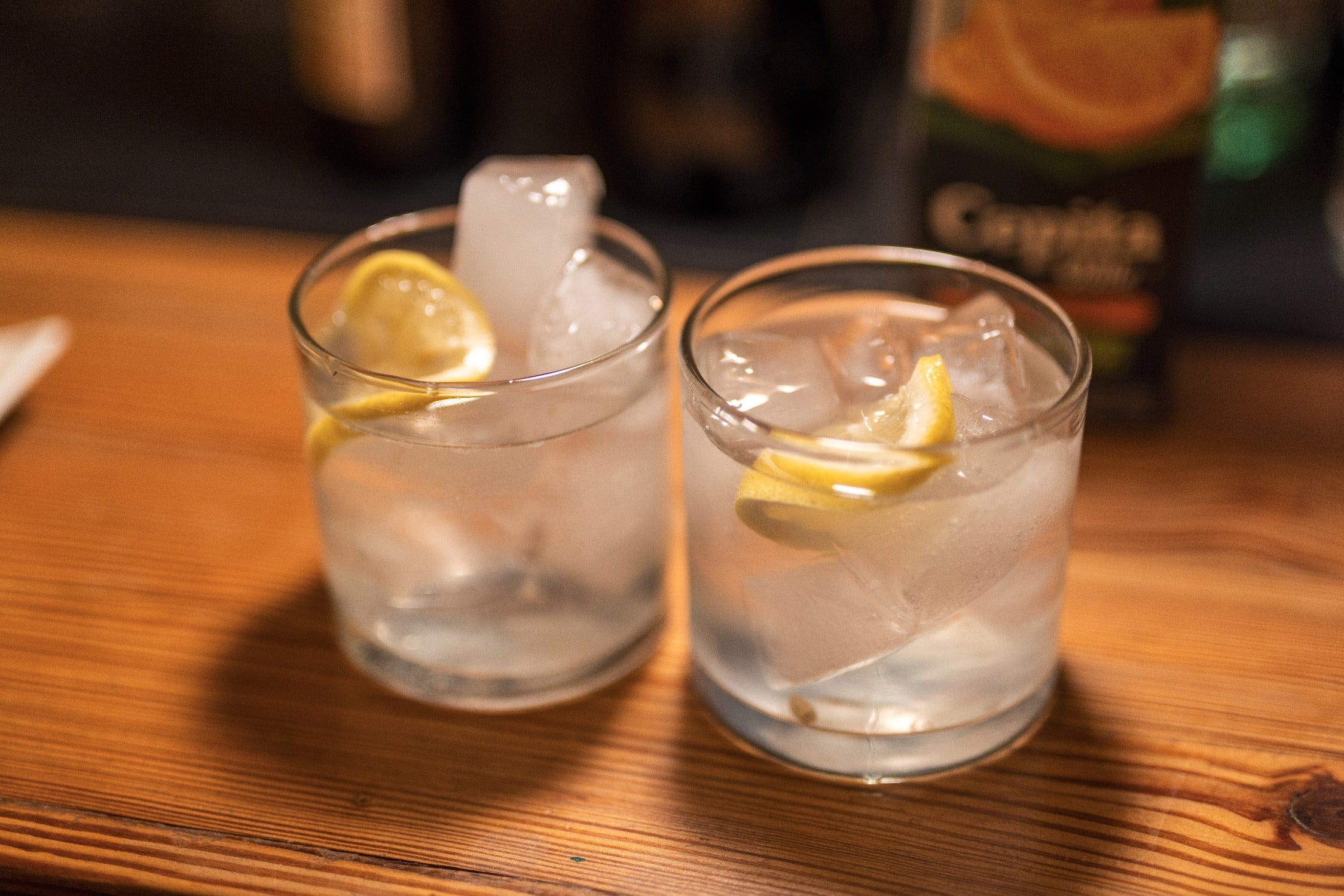 Two clear glass tumblers with ice and lemon wedges on a warm wooden table, lodge drink for Jurassic Lake trip