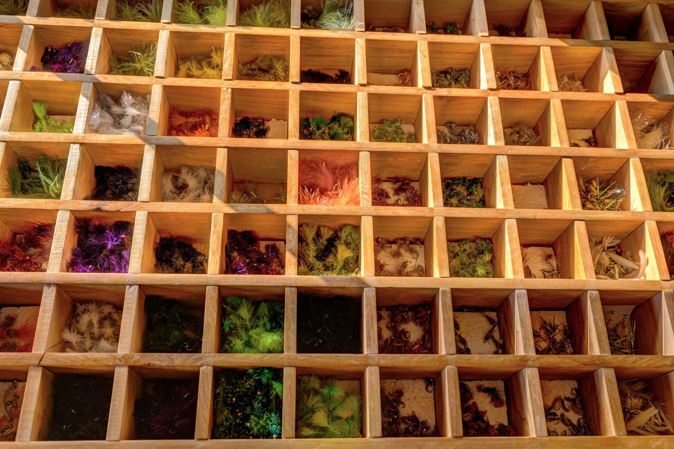 Warm wooden grid organizer with colorful feather fly fishing lures in small cubbies, rustic lodge decor