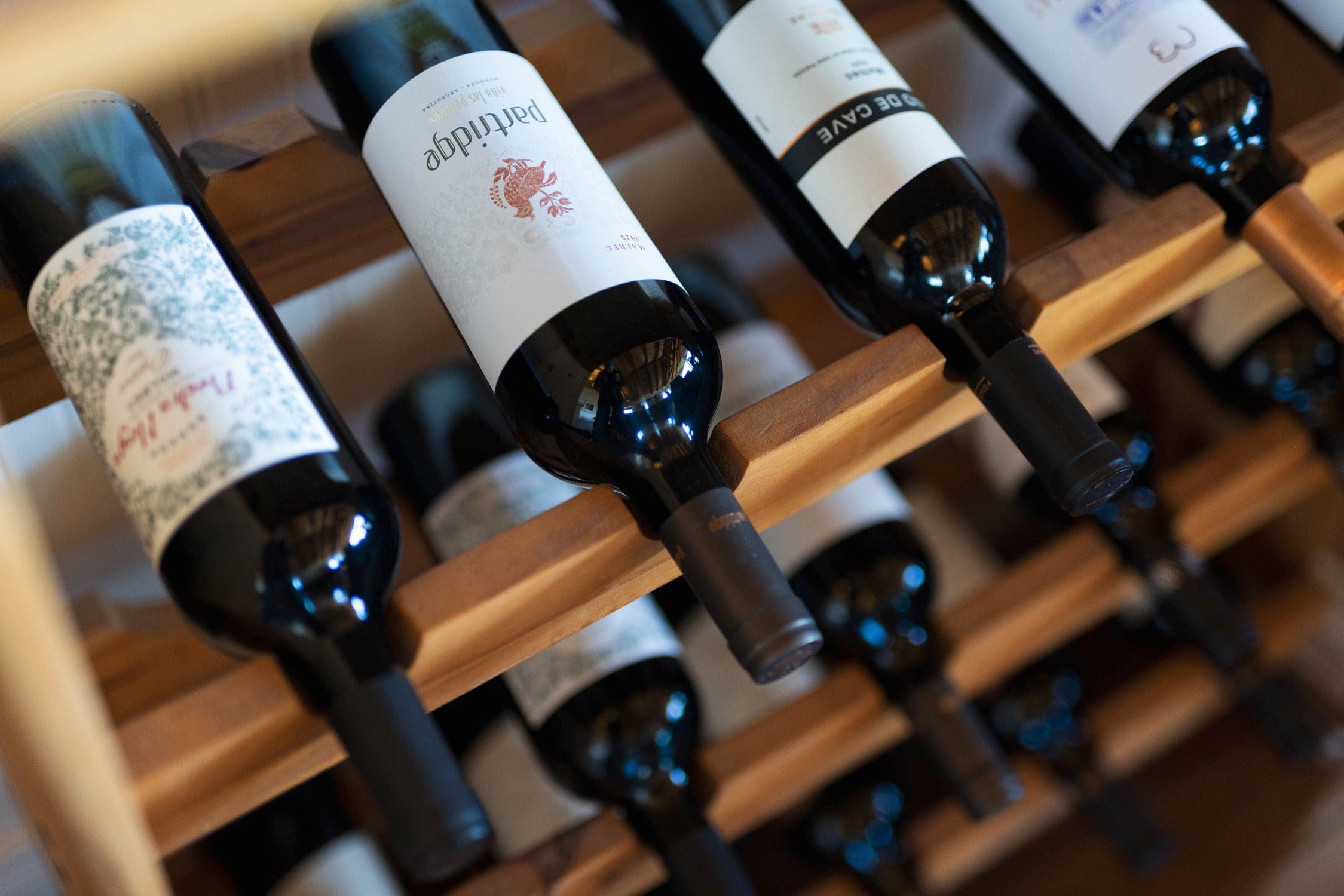 Dark glass wine bottles with white labels stored horizontally on a warm wood wine rack, rustic lodge display