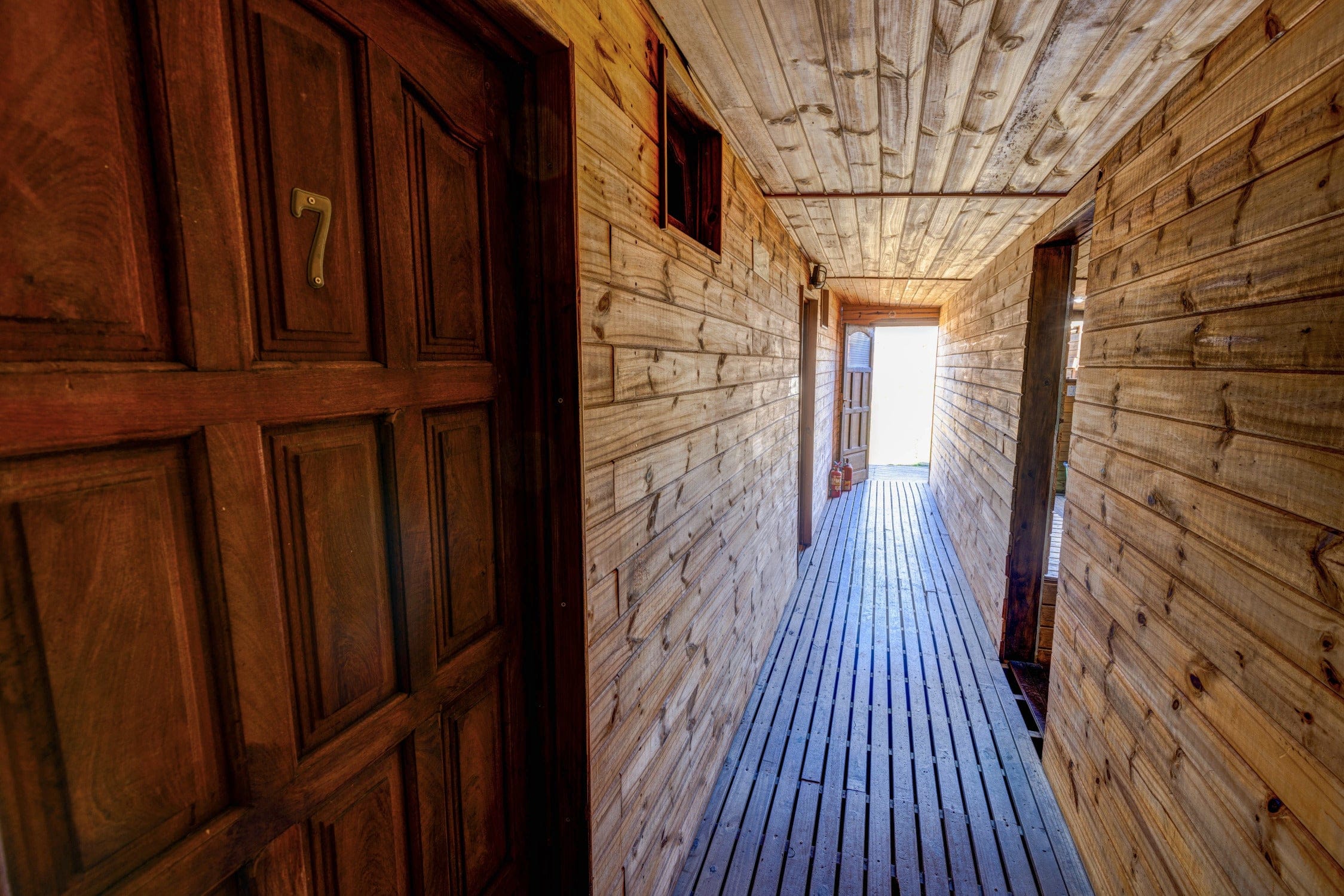 Warm wooden lodge corridor with slatted floor, plank walls and ceiling and carved dark door numbered 7