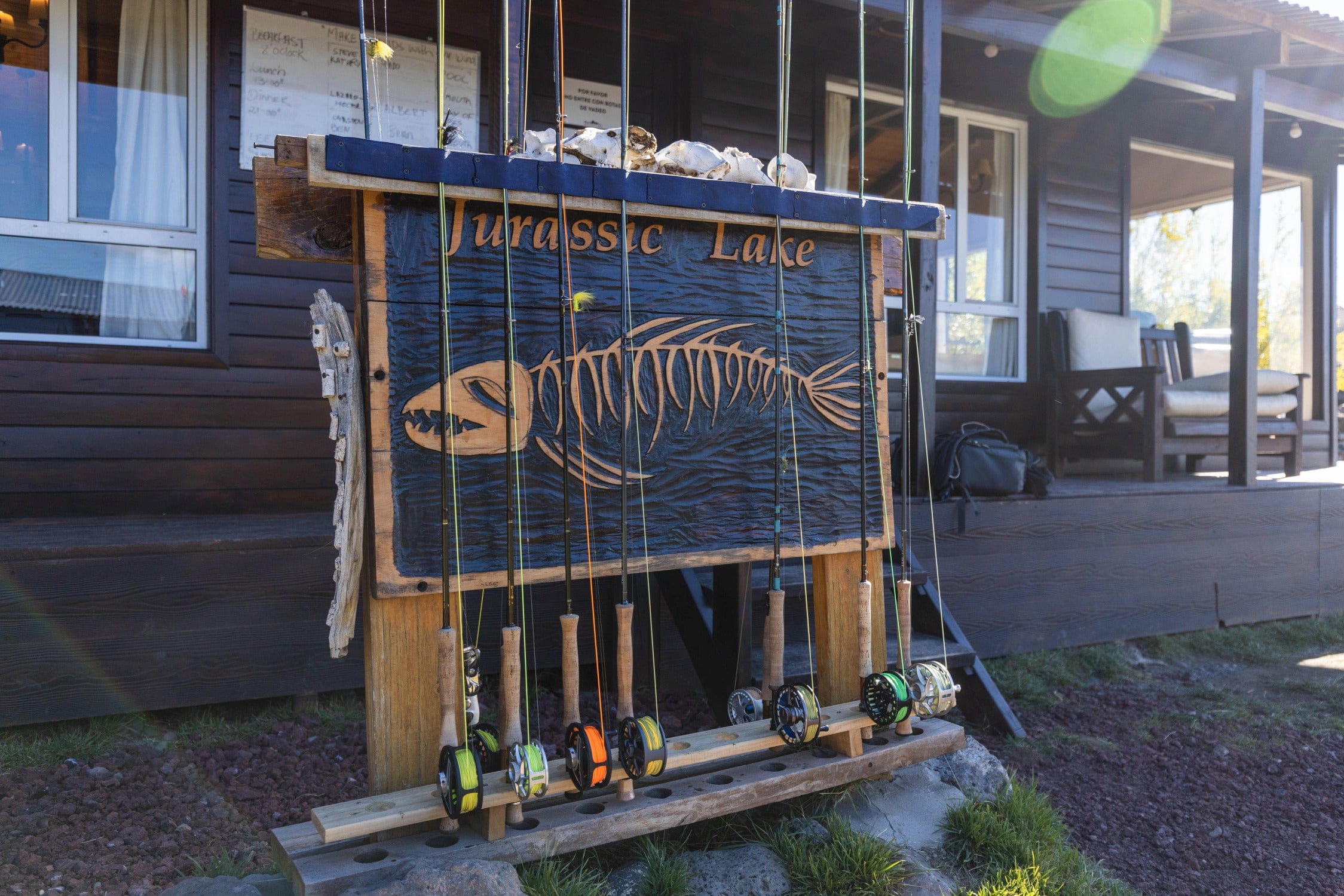 Rustic dark wood Jurassic Lake Lodge sign with orange carved fish skeleton and lined cork-handled fishing rods and reels